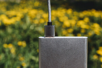 External battery with charging cable against a background of bright yellow flowers.