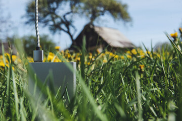 Silver power bank in green grass with a blurry rustic house background.
