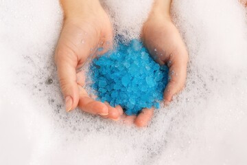 Hands holding blue bath salt in foam water