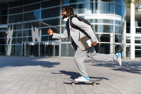 Professional in suit skateboarding with documents outdoors in urban setting