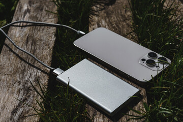 Portable Power Bank Charging Smartphone Outdoors on Wooden Surface