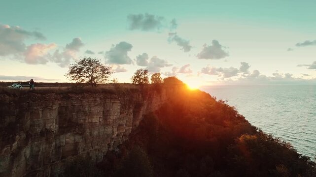 Silhouettes of a couple in love against the sunset. Aerial view of young couple huggin on cliff edge on sunset.