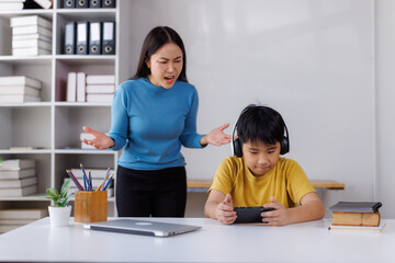 Asian mother scolding son playing videogames instead of studying