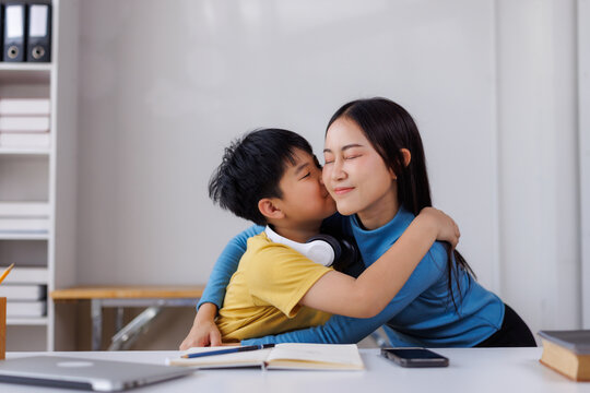 Asian boy kissing and hugging his homeschooling mother at her desk