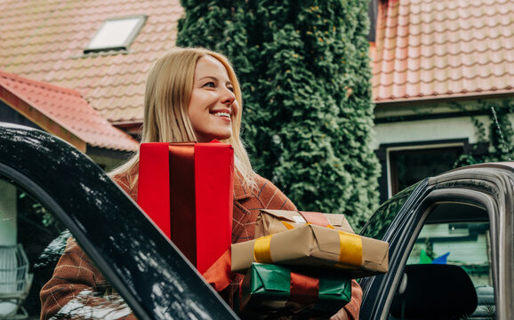 Smiling woman bringing Christmas gifts home by car during holiday