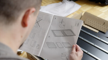 Man reading instructions while assembling cabinet furniture, over shoulder view