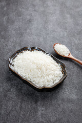 Fresh White Long Grain Rice in Glass Bowl with Wooden Spoon on Dark Background