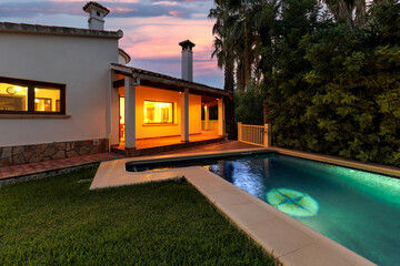 Evening view of a Mediterranean-style villa across an illuminated pool and green lawn.