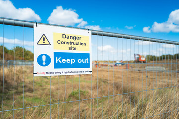 Shallow focus of a newly erected public Keep Out sign seen on a temeprroay fence at the boundary of a new, British, housing development project in Britain. The ground behind has been cleared.