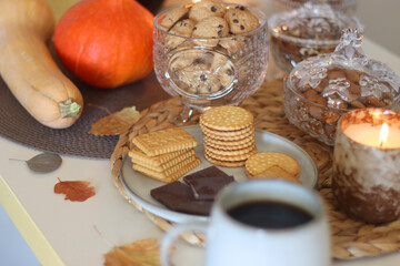 Lit candles, cookies, chocolate, nuts, tea, wine, pumpkins, books, reading glasses and autumn leaves on the table. Autumnal hygge at home. Selective focus.