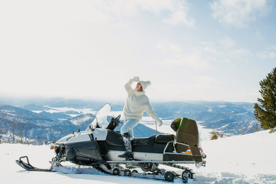 A woman in winter in the mountains on a snowmobile with a beautiful view
