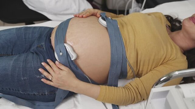 Beautiful young pregnant woman at electrocardiograph check up for baby health and expected date of birth. Fetal heart monitoring. Healthcare and medical service concept.