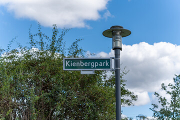 Kienberg Park Sign. A sign reading Kienberg Park stands against a blue sky. A street lamp rises next to it.