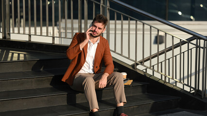 Fototapeta premium A white businessman in a neat, casual outfit looks displeased as he answers an urgent phone call during off-hours
