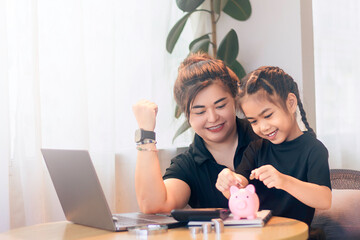 Fun savings lesson between mother and daughter at home with piggy bank and laptop during the day