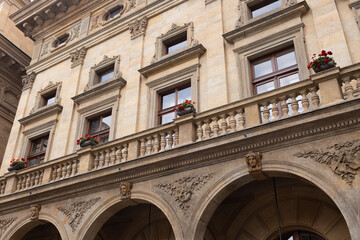 Obraz premium Architectural facade of a historic building featuring ornate stonework, decorative balconies, and vibrant flower pots, showcasing classic design elements and urban charm