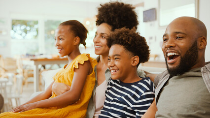 Family At Home Sitting On Sofa Together Watching A Show Or Movie To TV