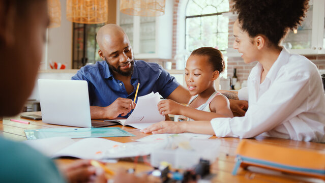 Family Around Table At Home Using Laptop With Parents Helping Children With Science Homework