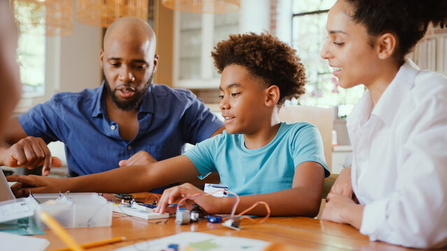 Family Around Table At Home Using Laptop With Parents Helping Children With Science Homework - Powered by Adobe