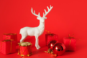 A festive composition featuring a delicate deer figurine surrounded by vibrant red gift boxes, set against a rich red background. 