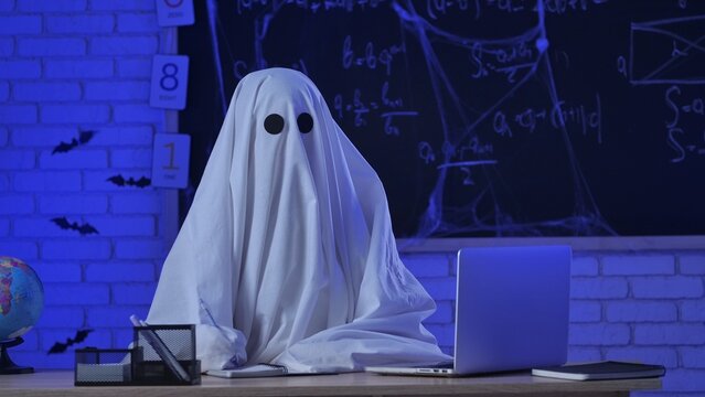 A person in a white ghost sheet sits at a table in a blue-lit room and writes with a pen in a notebook - Powered by Adobe