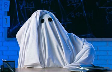 A man in a white ghost sheet sits at a table in a blue-lit room and clutches his head in despair