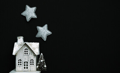 Miniature figure of a cute wooden house and sparkling stars on a black background.