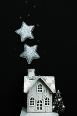 Miniature figure of a cute wooden house and sparkling stars on a black background. Top view, vertical image.