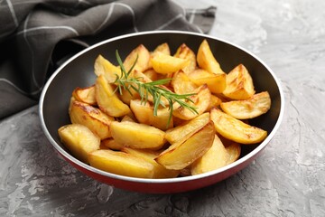 Tasty baked potatoes with rosemary in frying pan on grey textured table, closeup