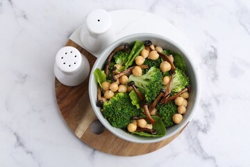 Delicious salad with shimeji mushrooms, chickpeas and broccoli in bowl on white marble table, top view
