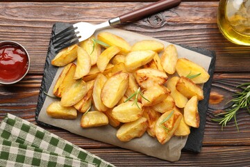 Tasty baked potatoes with rosemary, peppercorns and ketchup served on wooden table, flat lay