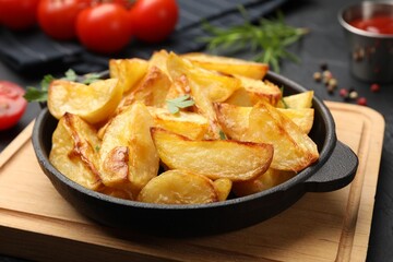 Tasty baked potatoes with parsley in frying pan on dark table, closeup
