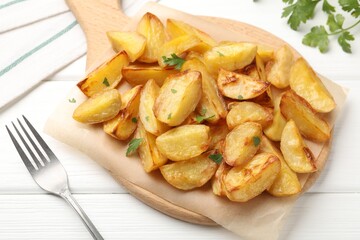 Tasty baked potatoes with parsley and fork on white wooden table, above view