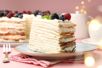 Piece of tasty crepe cake with berries served on pink wooden table against blurred lights, closeup