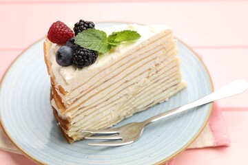 Piece of tasty crepe cake with berries served on pink wooden table, closeup