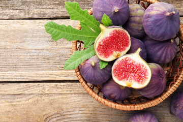 Fresh ripe figs and green leaf in basket on wooden table, top view. Space for text