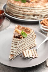 Piece of tasty crepe cake with cocoa powder, chocolate and nuts served on light table, closeup