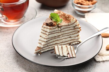 Piece of tasty crepe cake with cocoa powder, chocolate and nuts served on light table, closeup