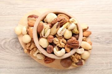 Mix of different nuts in bowl on wooden table, top view