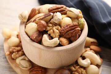 Mix of different nuts in bowl on wooden table, closeup