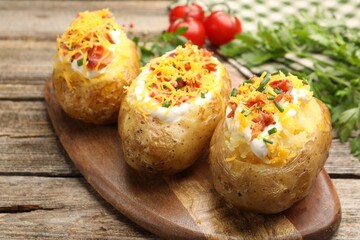 Tasty baked potatoes with sour cream, green onion, cheese and bacon on wooden table, closeup