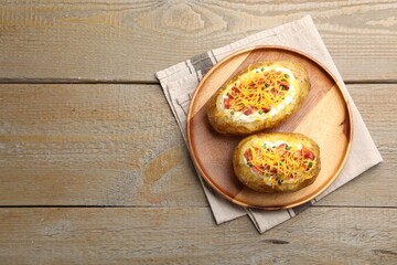 Tasty baked potatoes with sour cream, green onion, cheese and bacon on wooden table, top view. Space for text