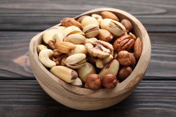 Mix of different nuts in bowl on wooden table, closeup