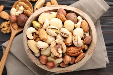 Mix of different nuts in bowl and spoon on wooden table, flat lay
