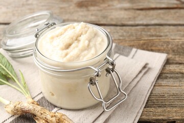 Tasty horseradish sauce and roots on wooden table, closeup