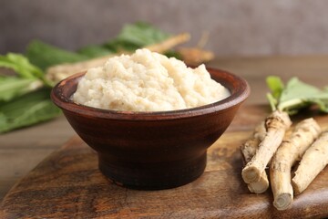 Tasty horseradish sauce and roots on wooden table, closeup