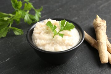 Tasty horseradish sauce with parsley and roots on black table, closeup