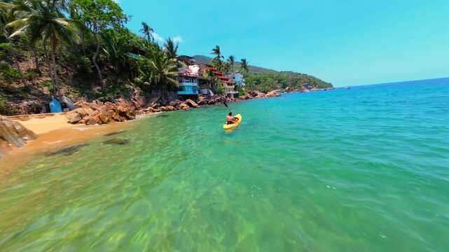 FPV drone flyby young kayaker paddling near rocky shore in Yelapa, M&eacute;xico