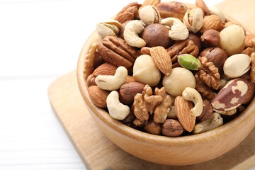 Mix of different nuts in bowl on white table, closeup. Space for text