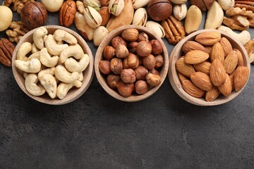 Mix of different nuts in bowls on grey table, flat lay. Space for text